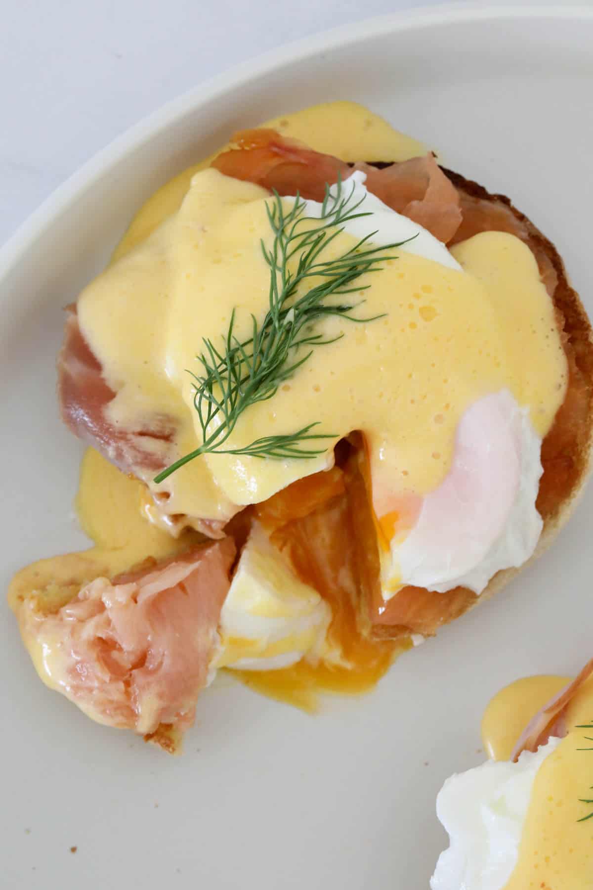 Hollandaise sauce over a muffin served with bacon and eggs, and a sprig of dill on top.