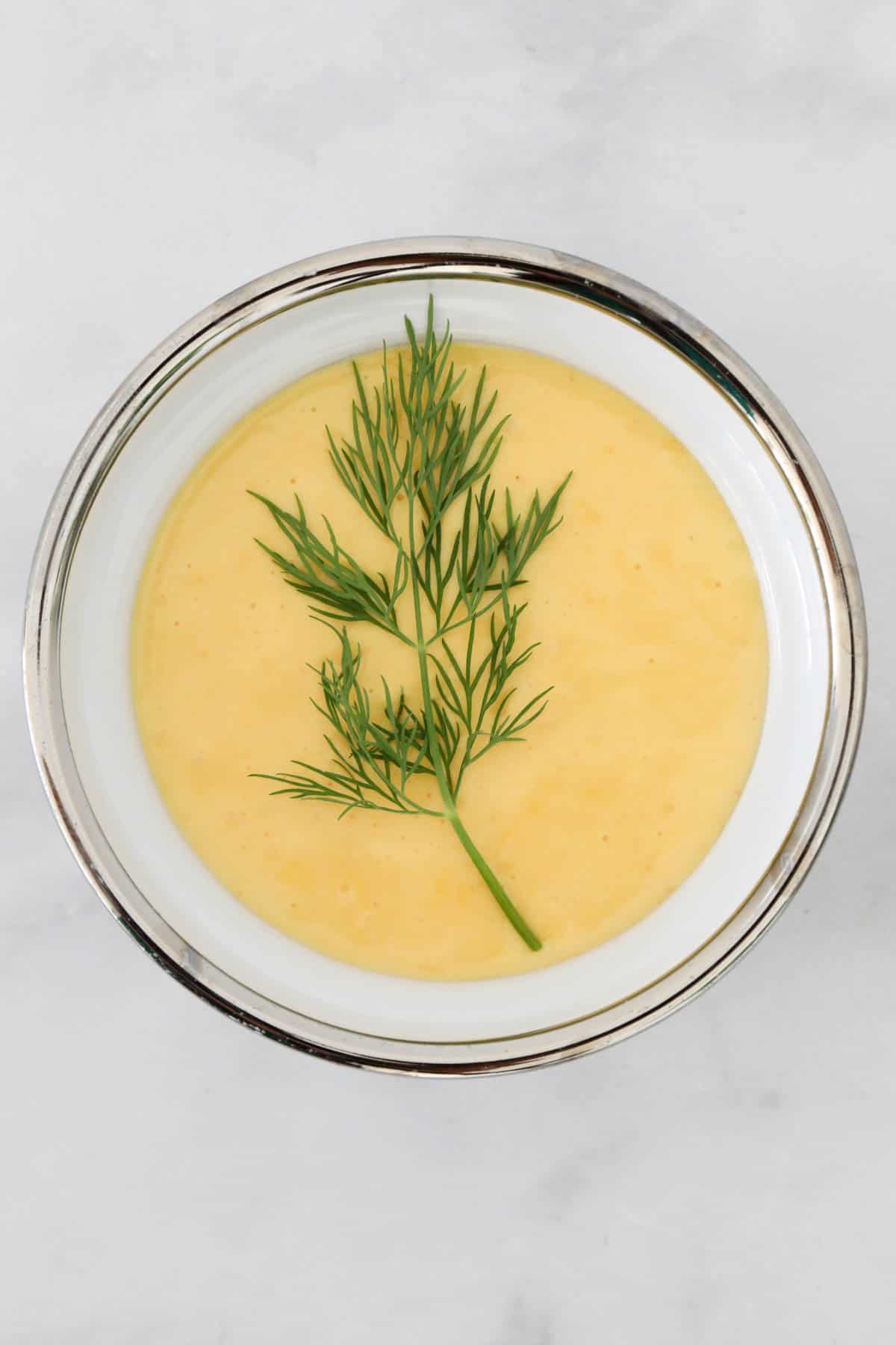 Hollandaise sauce in a bowl decorated with a sprig of dill.