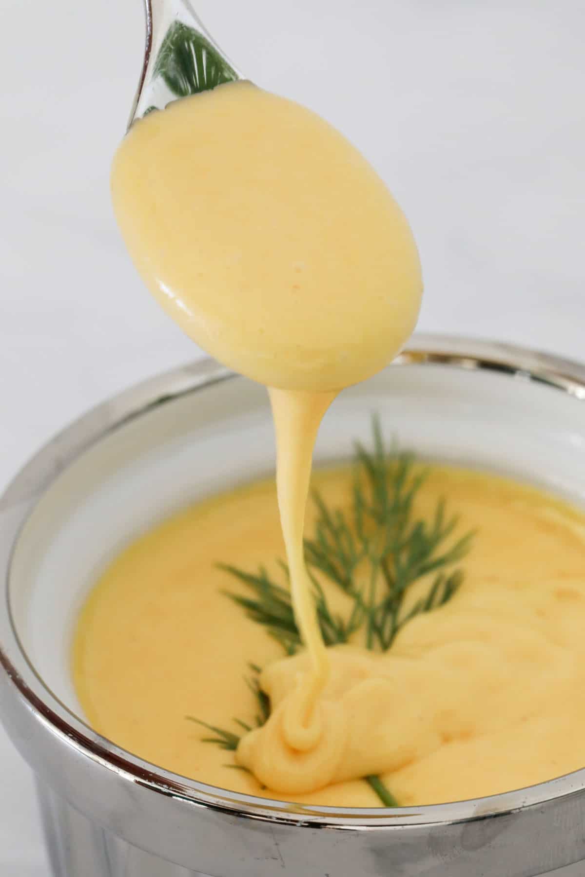 A spoon poured hollandaise sauce into a bowl.