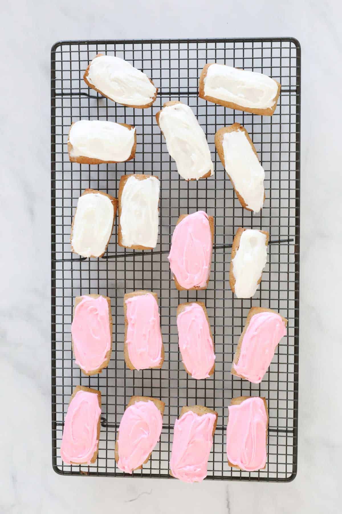 The pink and white iced cookies on a metal cooling rack.