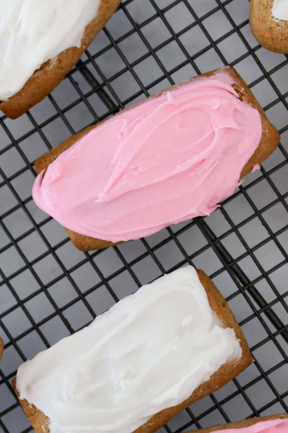 Close up of an pink iced honey jumble cookie on metal cooling rack.