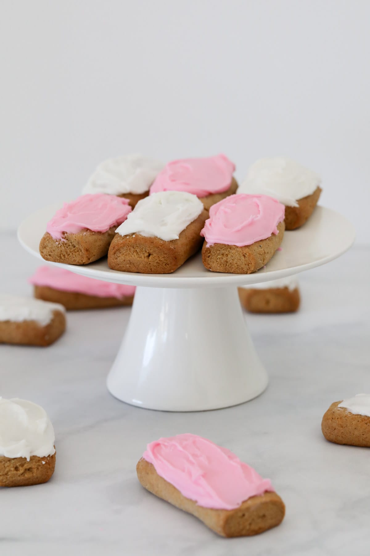 A cake stand with pink and white iced honey jumbles on it, with more honey jumbles at the base.