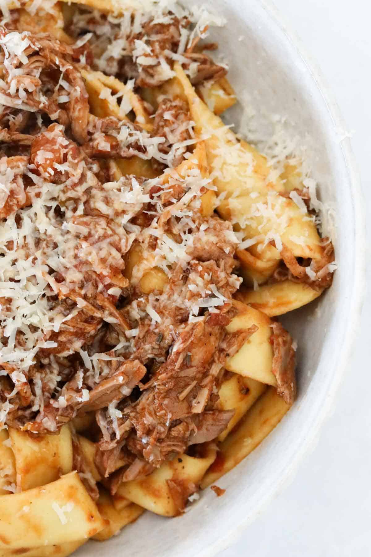 A bowl of lamb ragu with pappardelle and grated parmesan cheese.