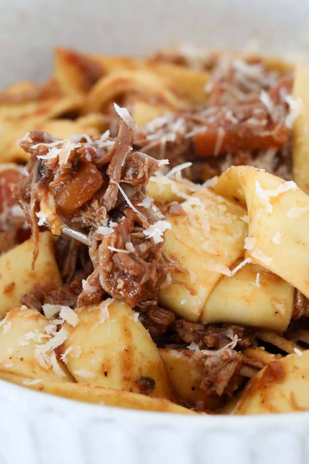 A fork holding up a mouthful of lamb ragu over thick ribbons of parpadelle.