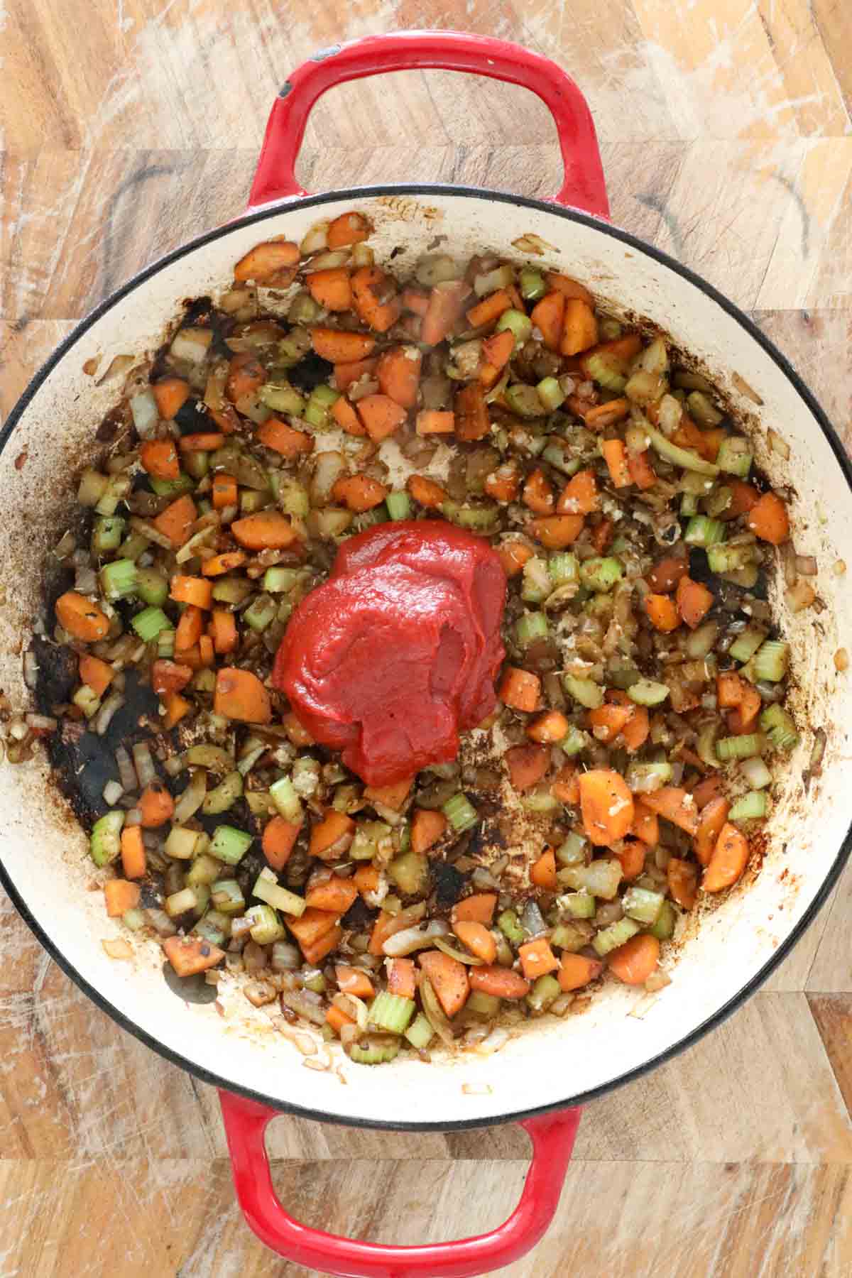 Tomato paste added to the vegetables in a pan.