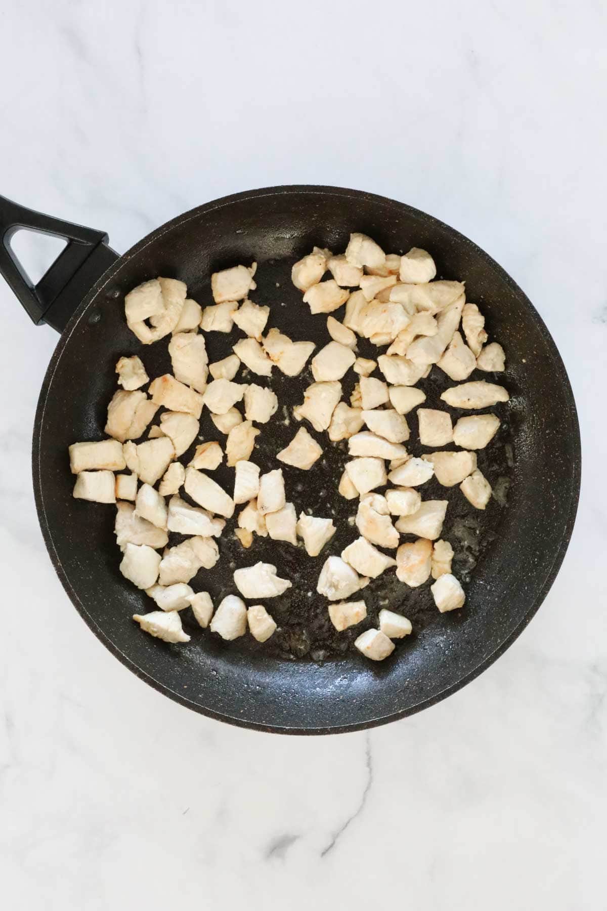 Cooked cubed chicken in a frying pan.