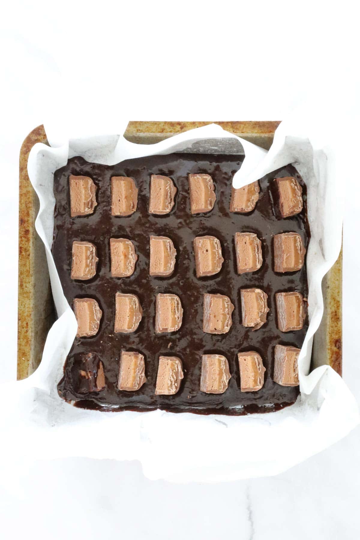 Pieces of Mars Bar placed over brownie batter in baking tin.