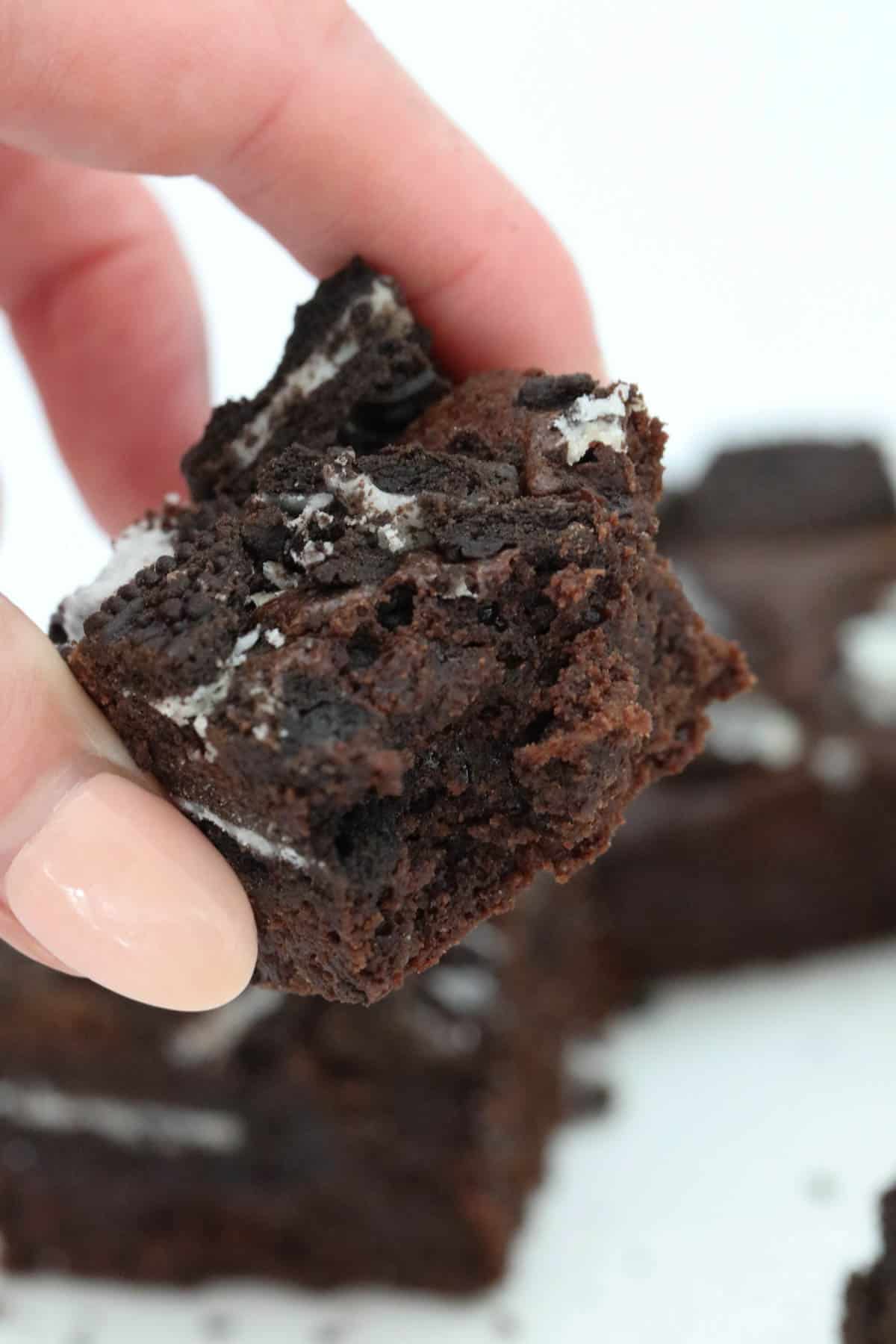 A hand holding a square of brownie to show the fudgy centre.