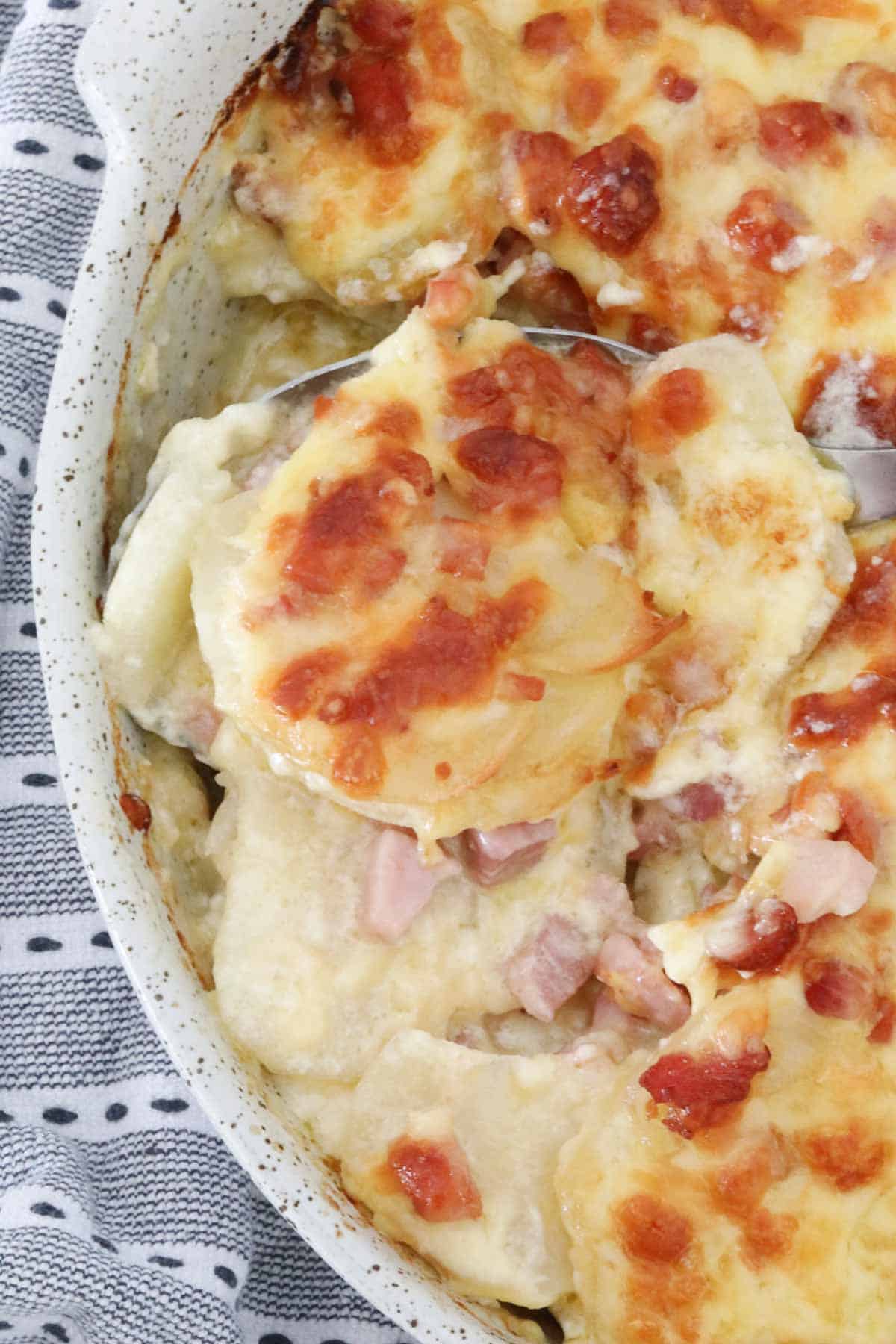 A spoon holding up a portion of the potato and bacon bake.