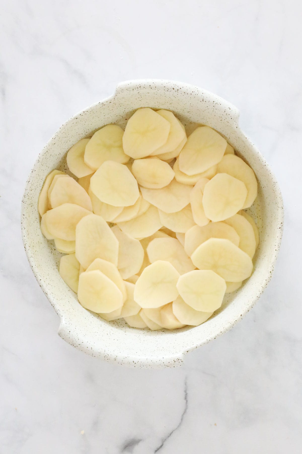 A third of the sliced potatoes layered in the bottom of the baking dish.