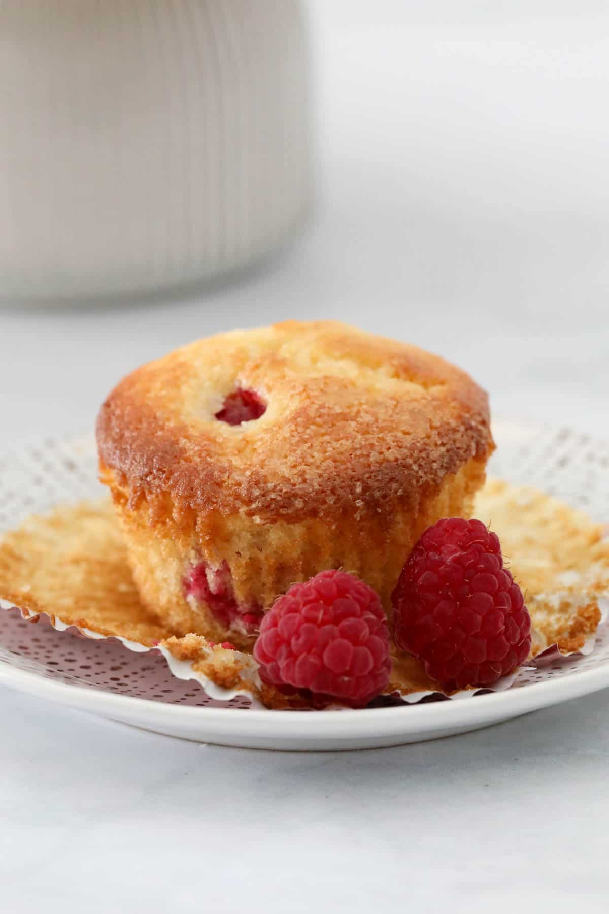 A muffin on a plate with fresh raspberries beside.