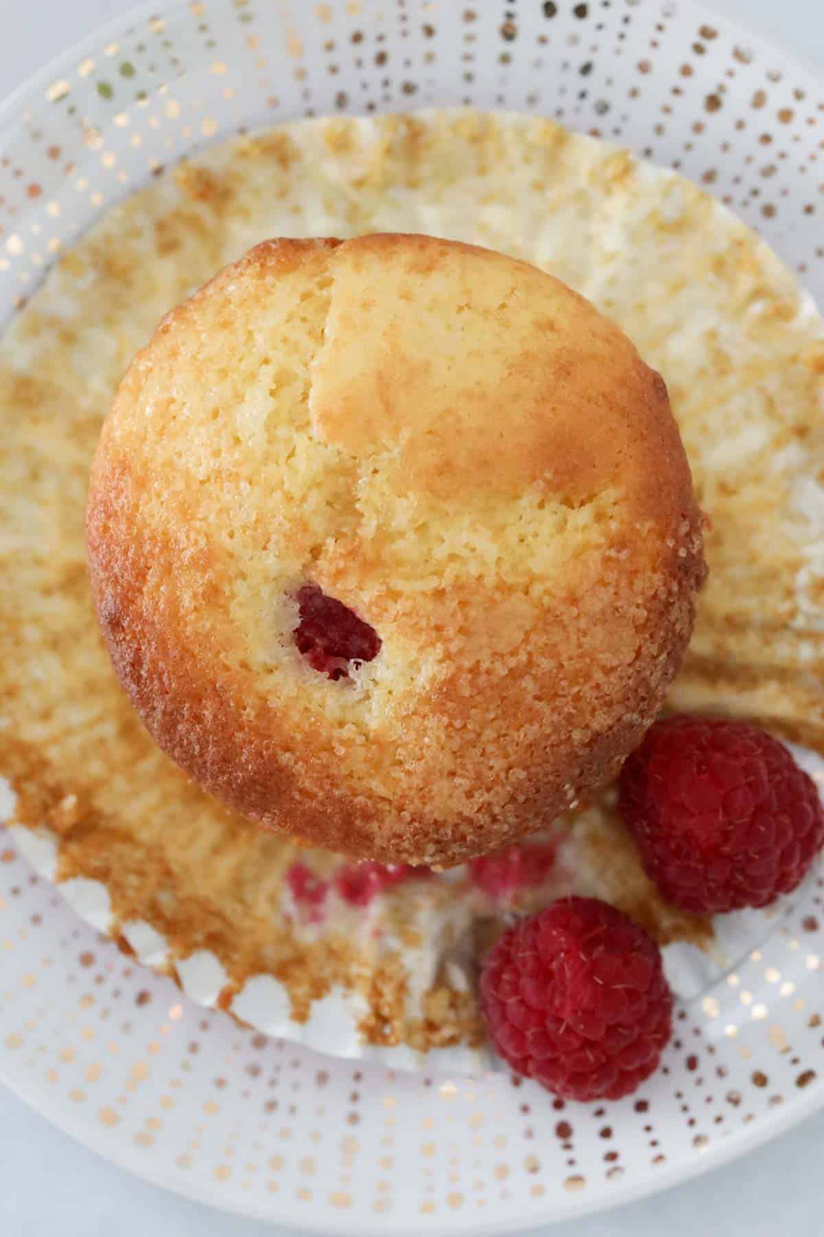 A muffin with the case peeled back and two fresh raspberries beside.