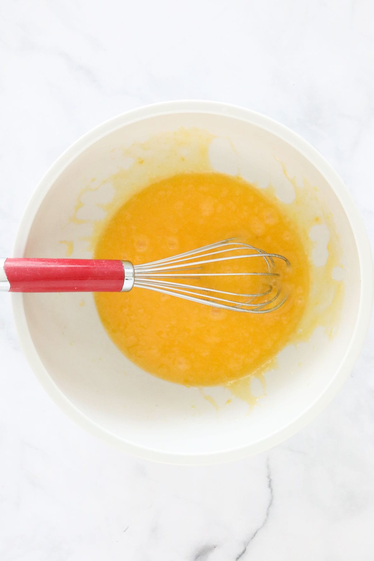 Oil, egg and sugar whisked together in a mixing bowl.