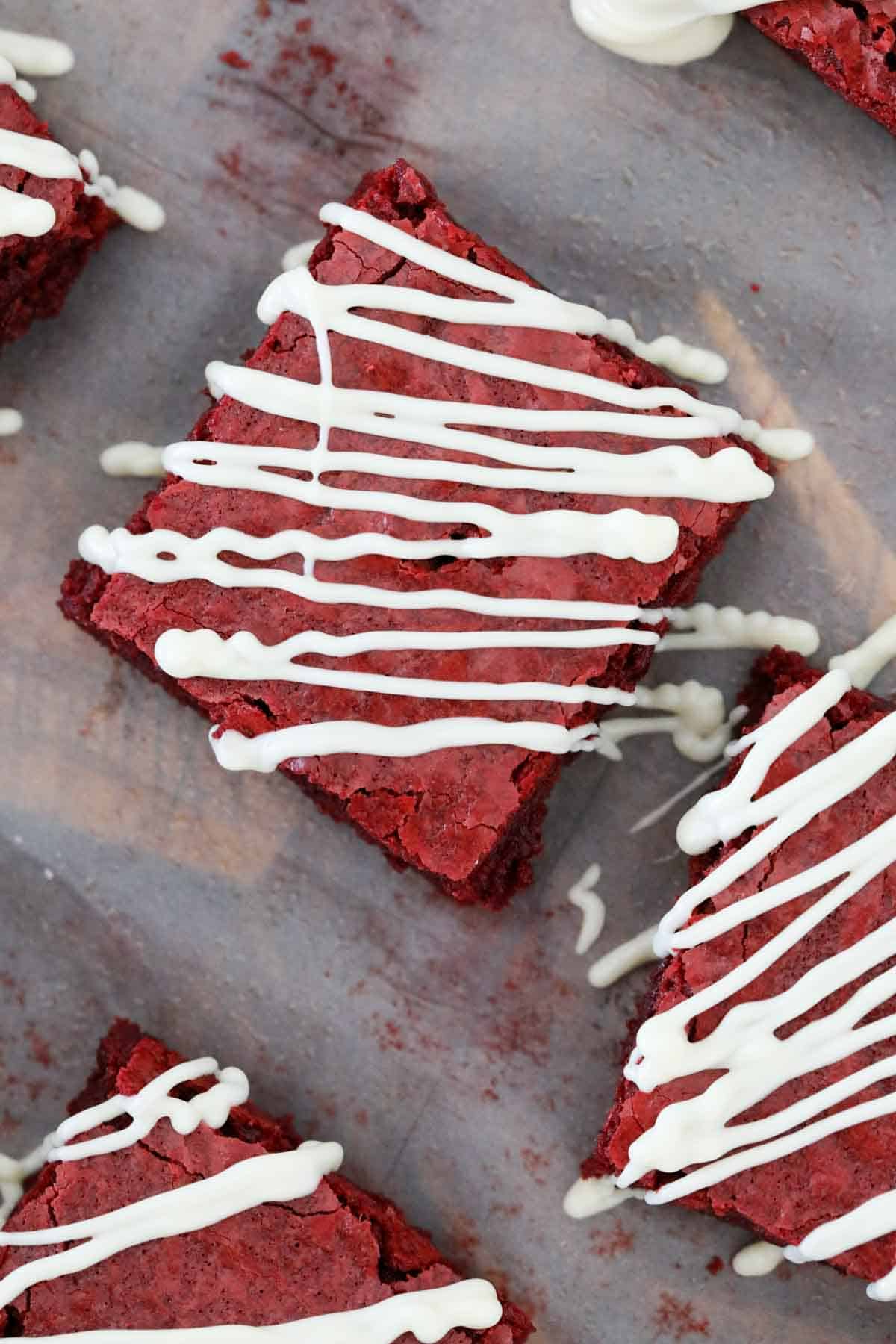 overhead shot of red brownies on baking paper after being drizzled with white chocolate.