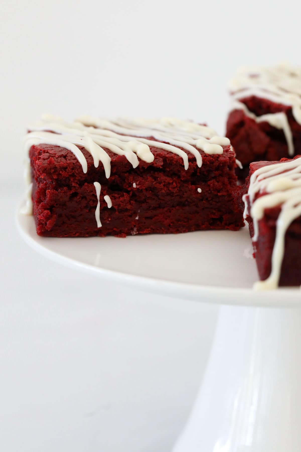 Close up of pieces of red velvet brownie on a white cake stand.