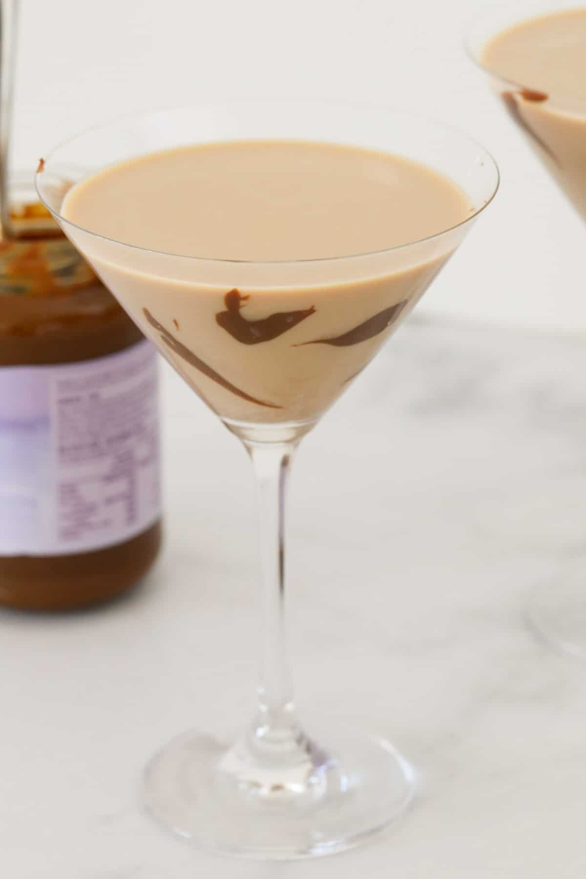 A glass of salted caramel cocktail in front of a jar of caramel sauce.