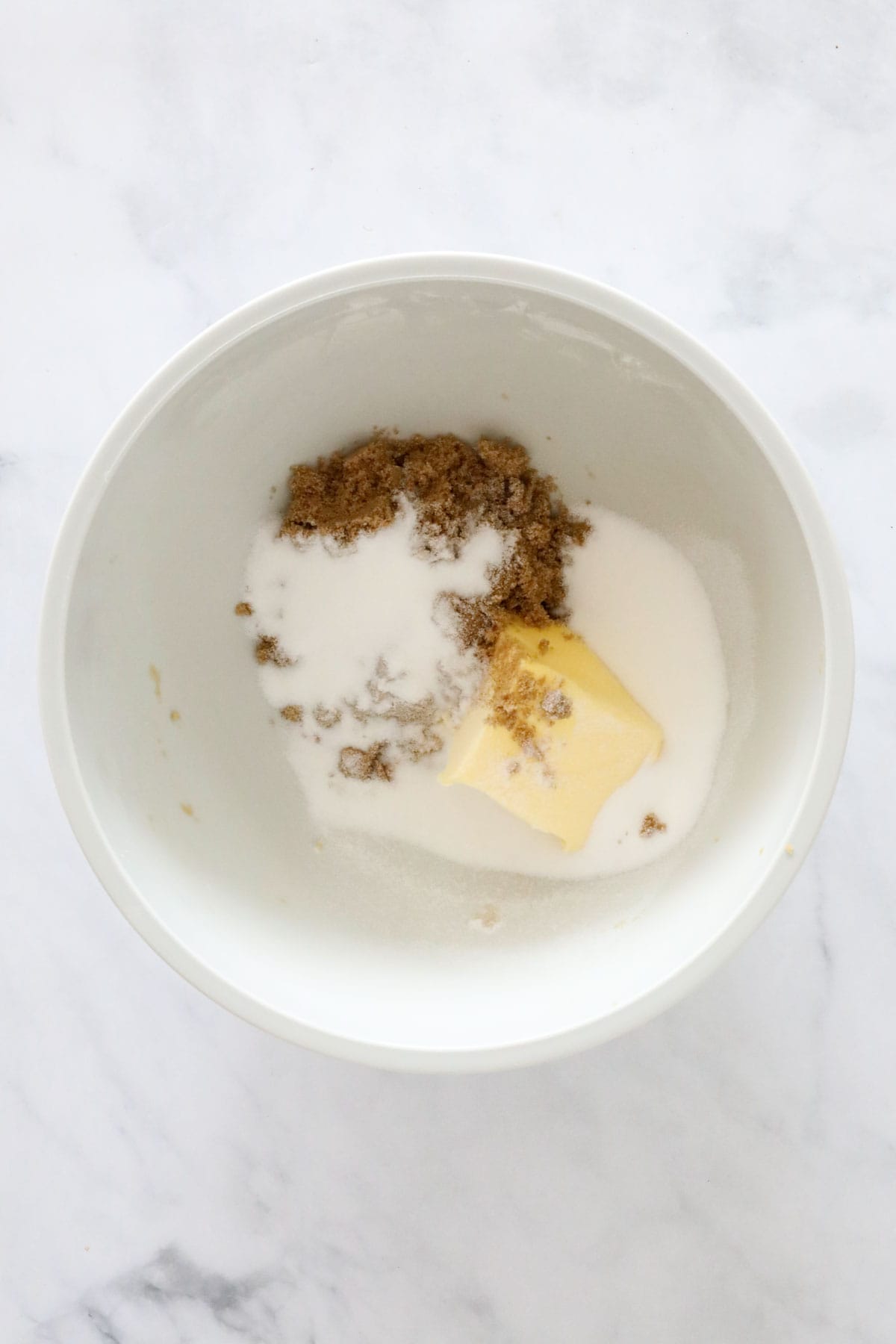 Butter and sugars in a white mixing bowl.