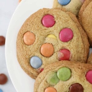 Soft and chewy cookies topped with colourful Smarties on a white plate.