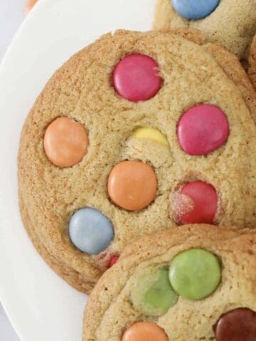 Soft and chewy cookies topped with colourful Smarties on a white plate.