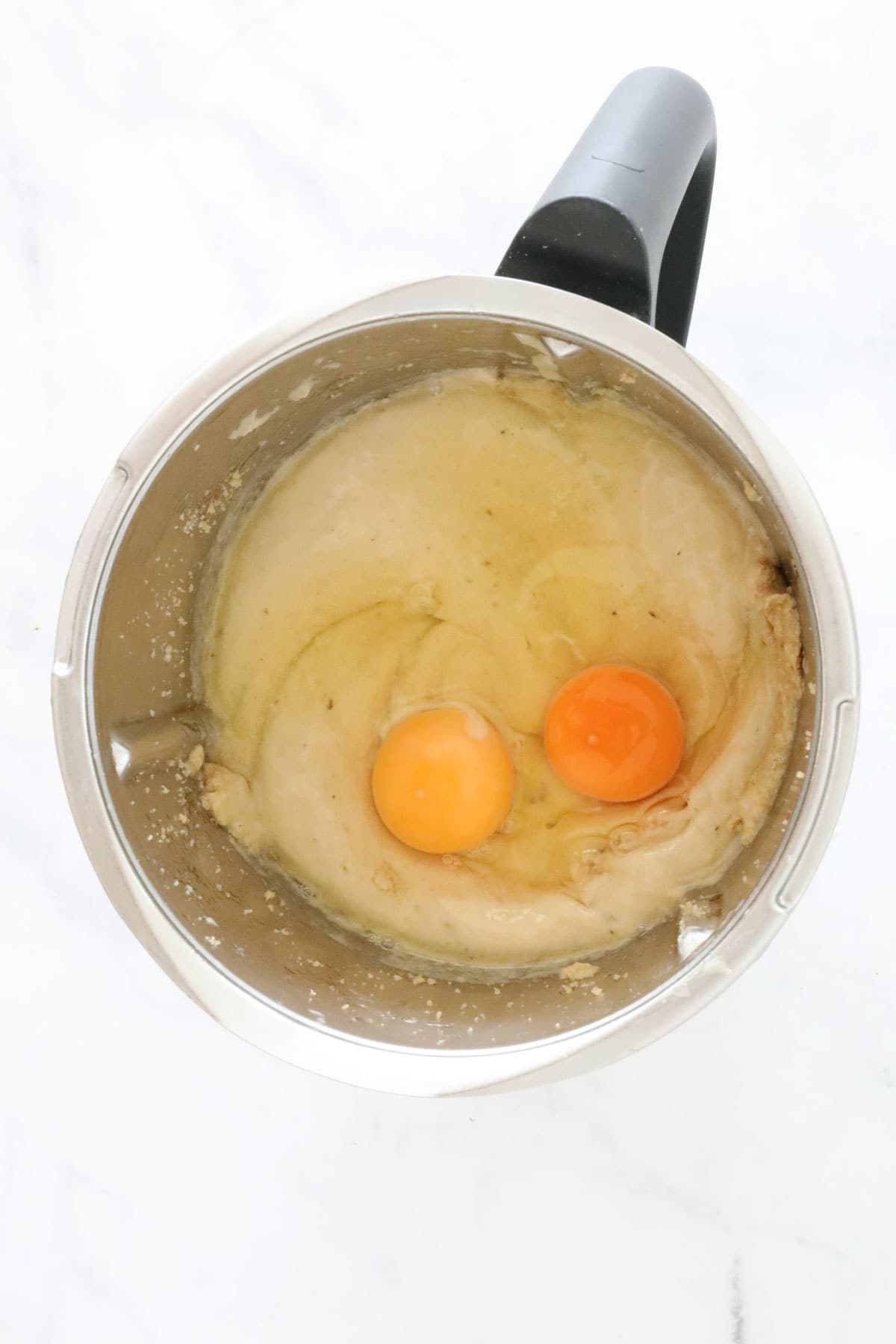 Two eggs on top of a creamy mixture in a Thermomix bowl.