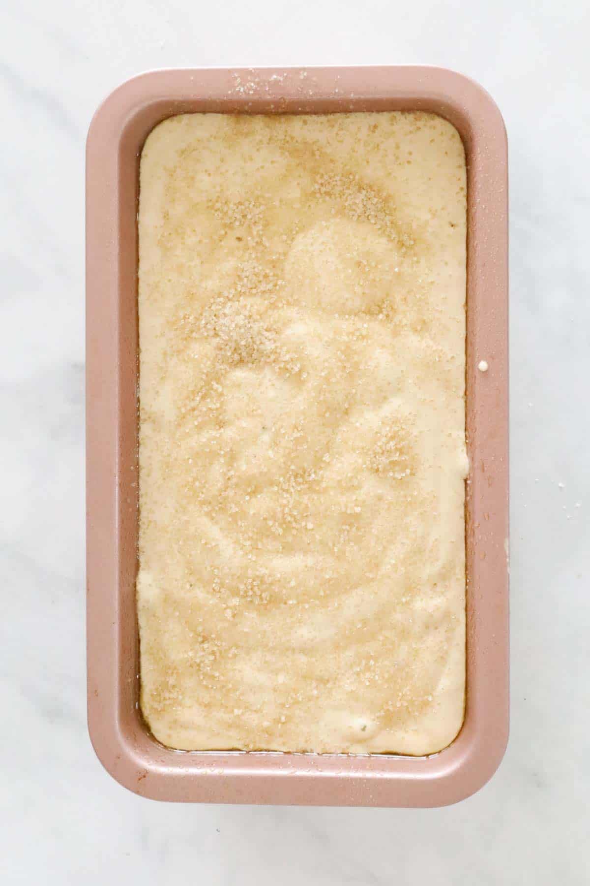 Banana bread mixture sprinkled with raw sugar, in a loaf tin.