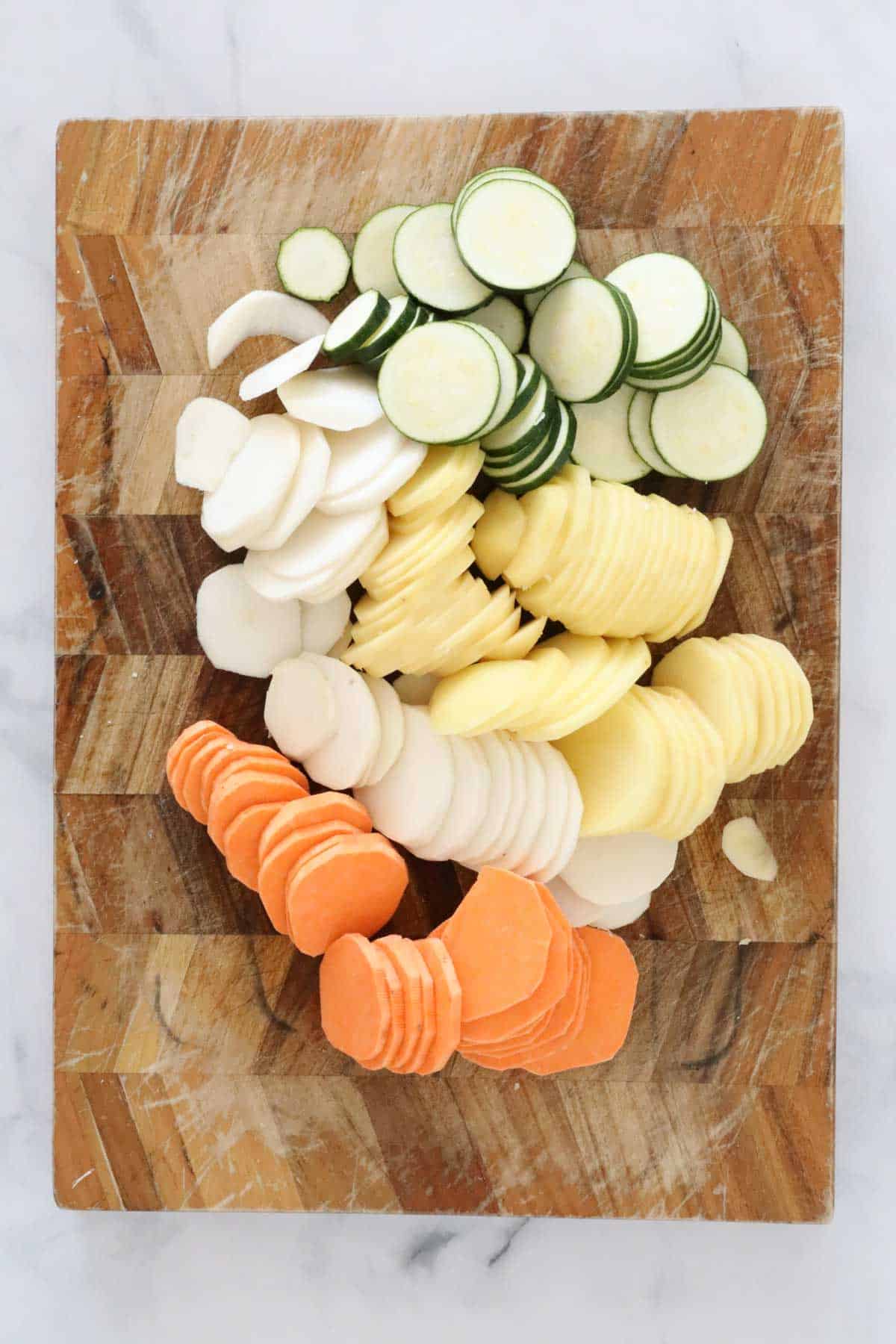 Thinly sliced vegetables on a wooden chopping board.