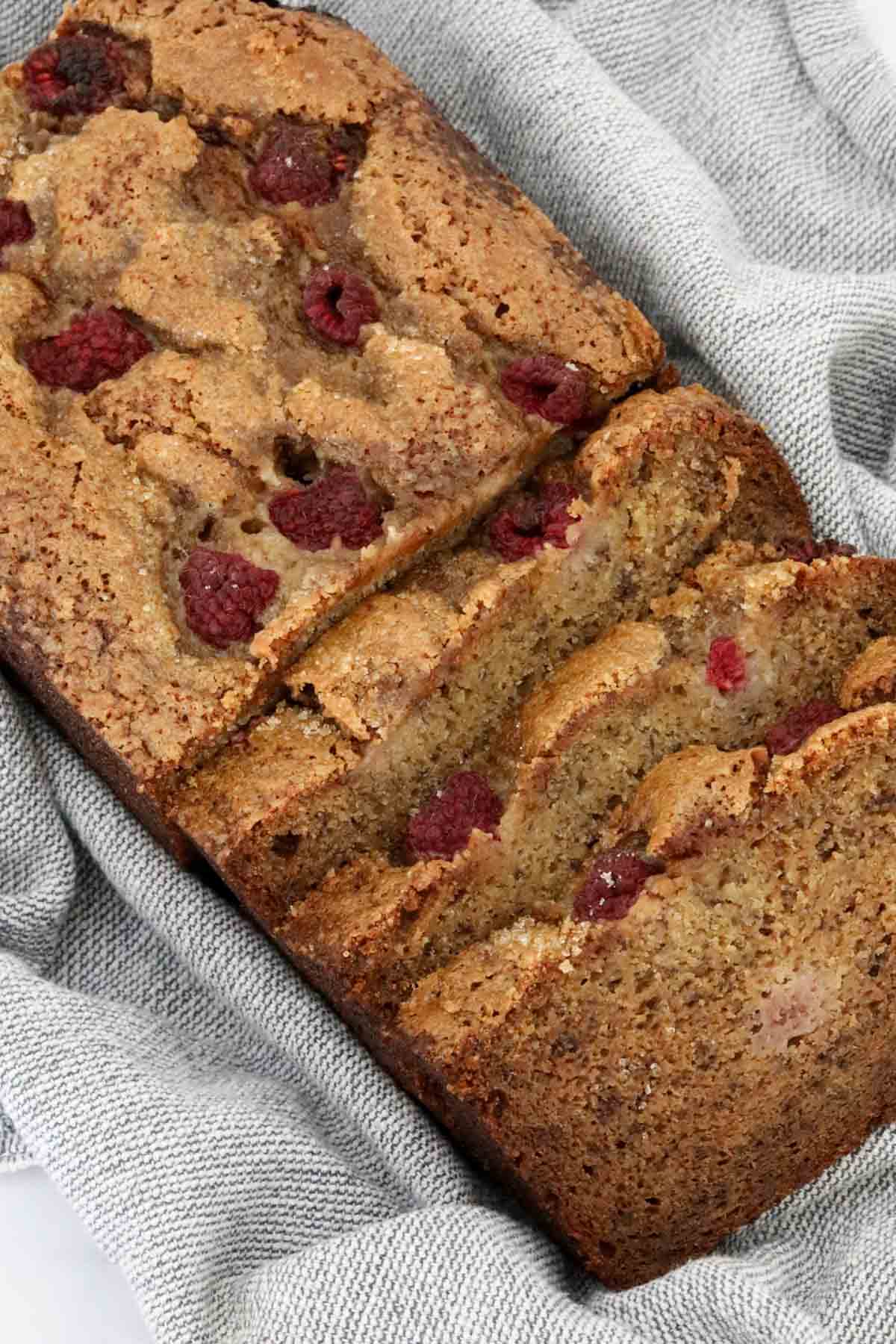 A loaf of banana bread with raspberries with three slices cut.