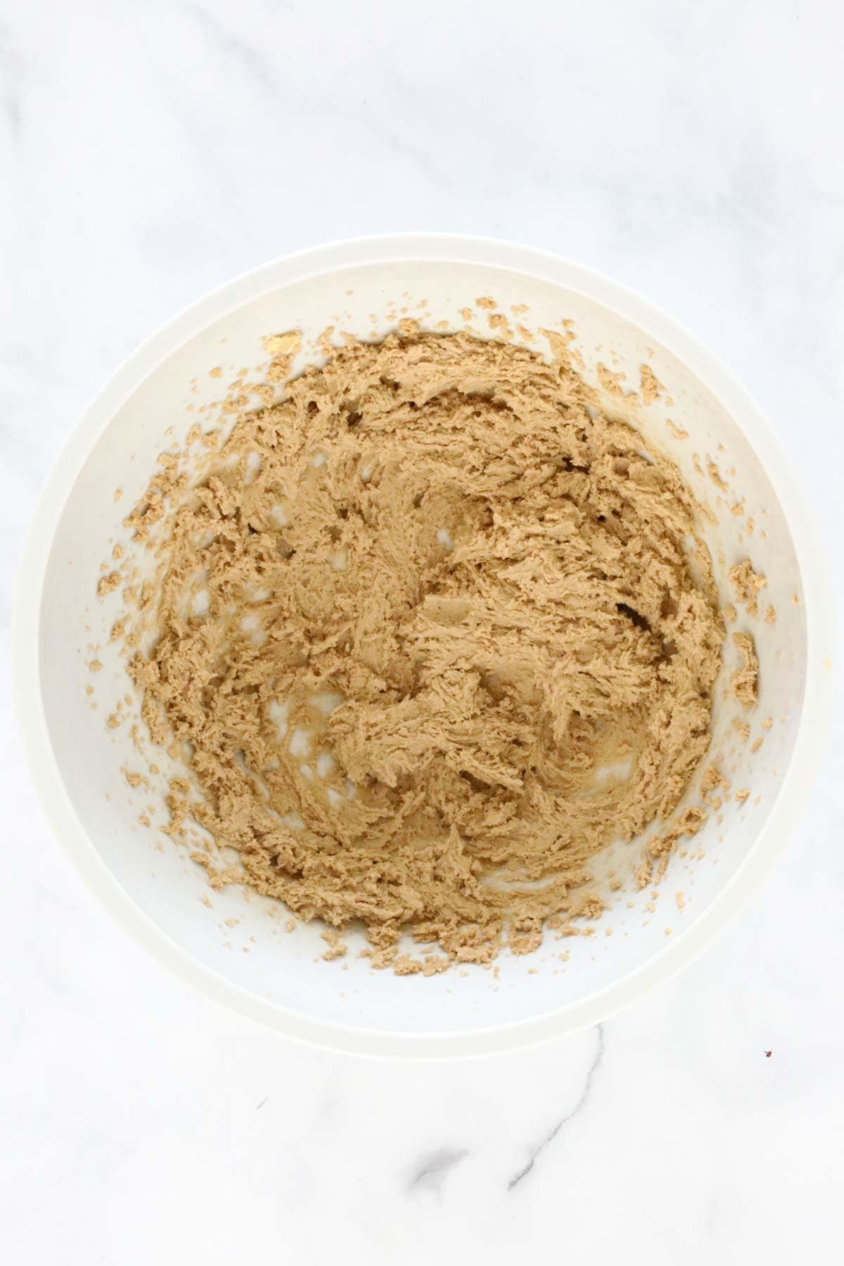 Butter and brown sugar creamed in a white mixing bowl.