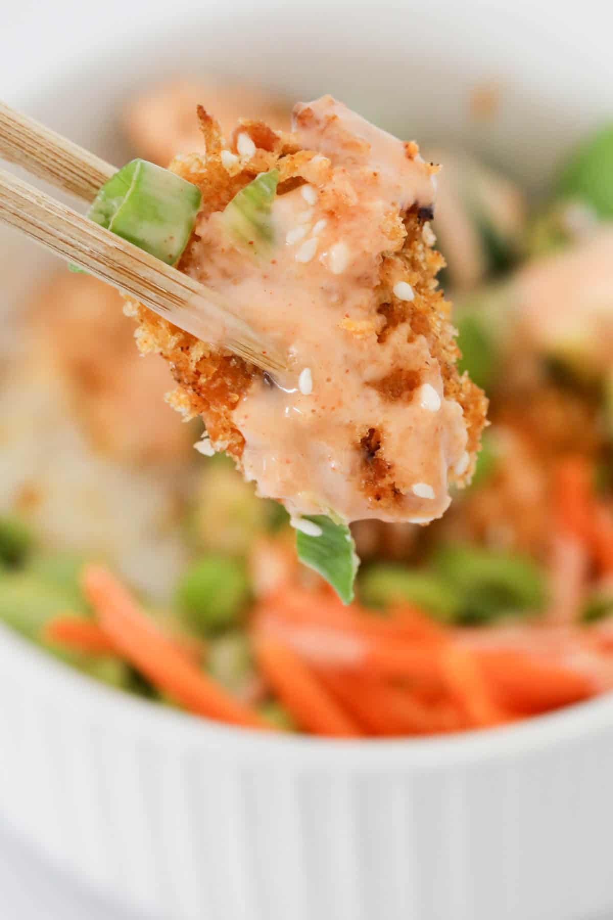 Close up of a piece of crunchy crumbed chicken held with chopsticks.