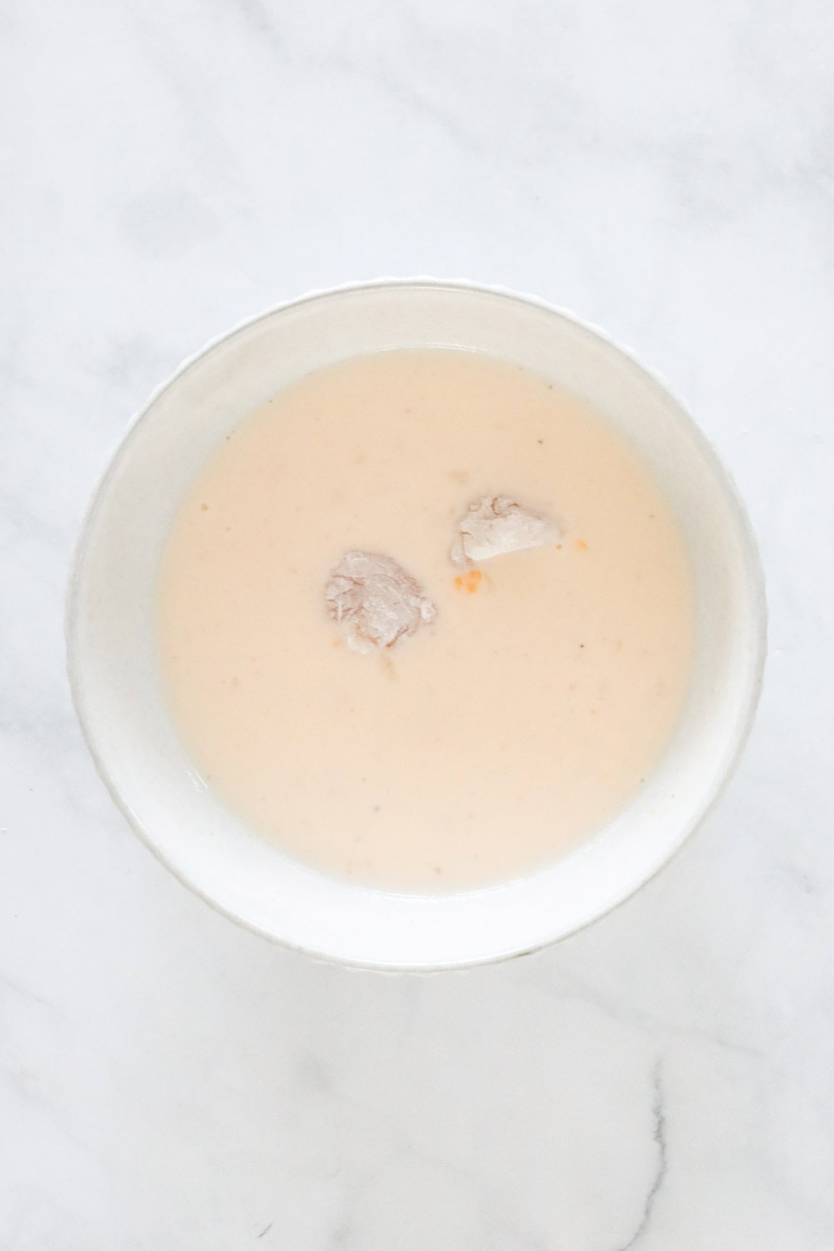 Coated chicken pieces in a bowl of buttermilk mixture.