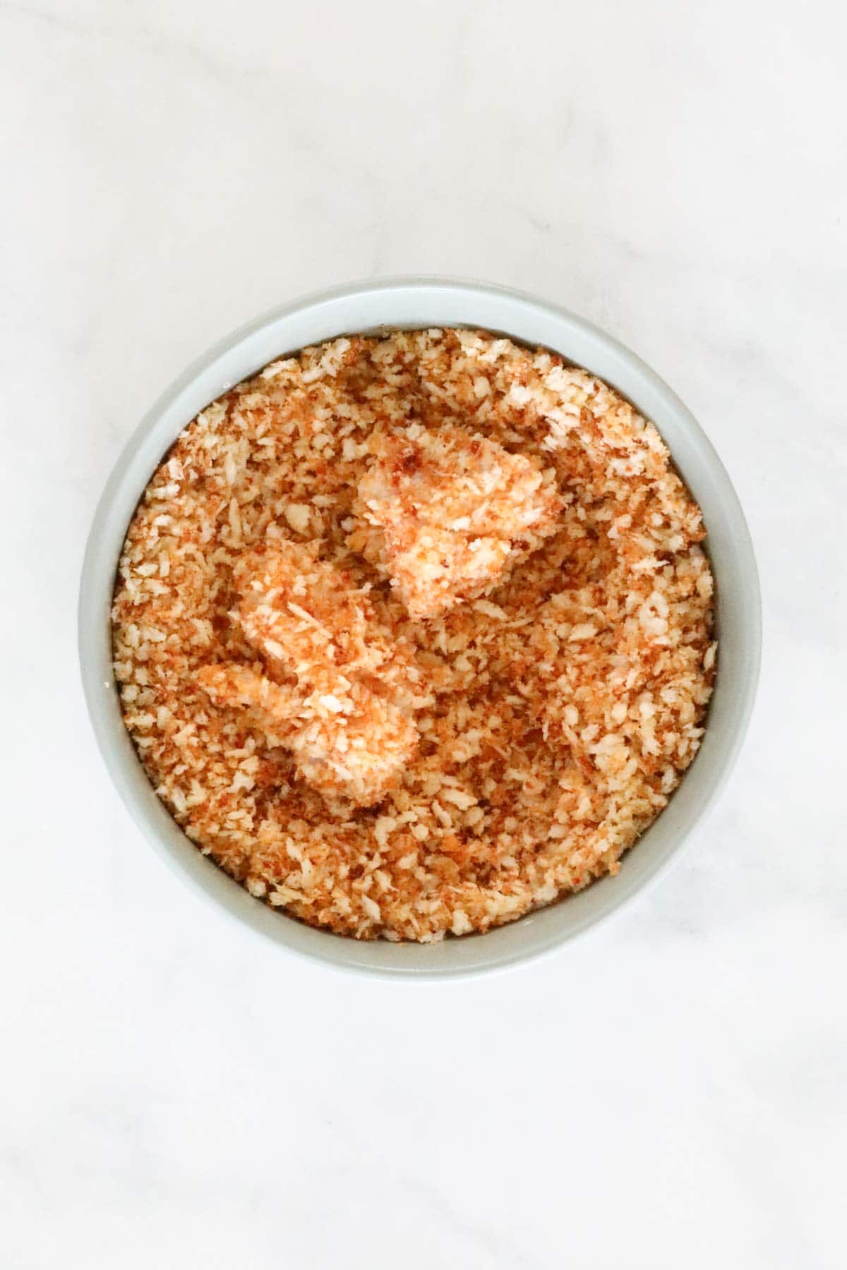 The chicken pieces in a bowl of seasoned panko crumbs.