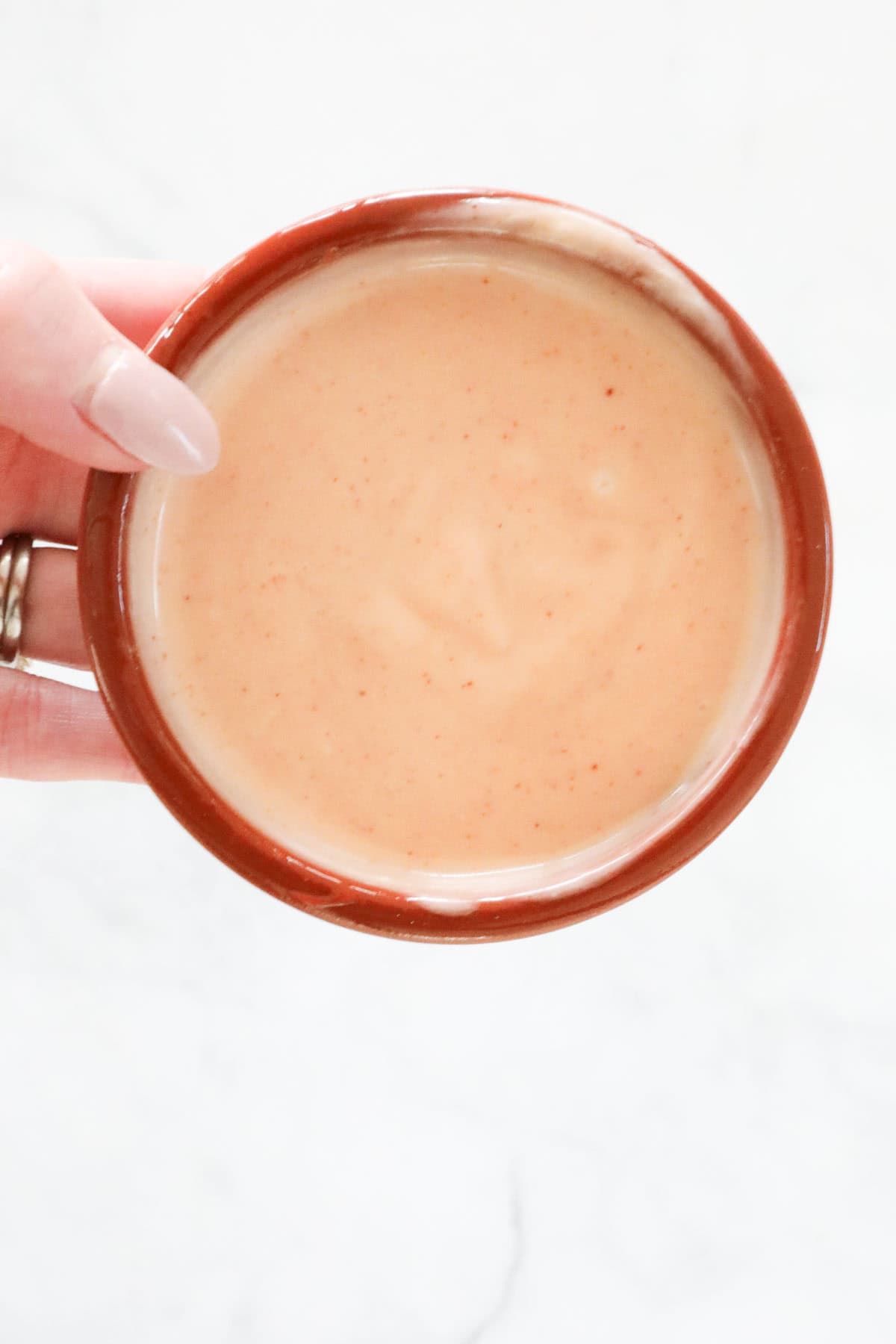 A hand holding a small bowl of the mixed bang bang sauce.