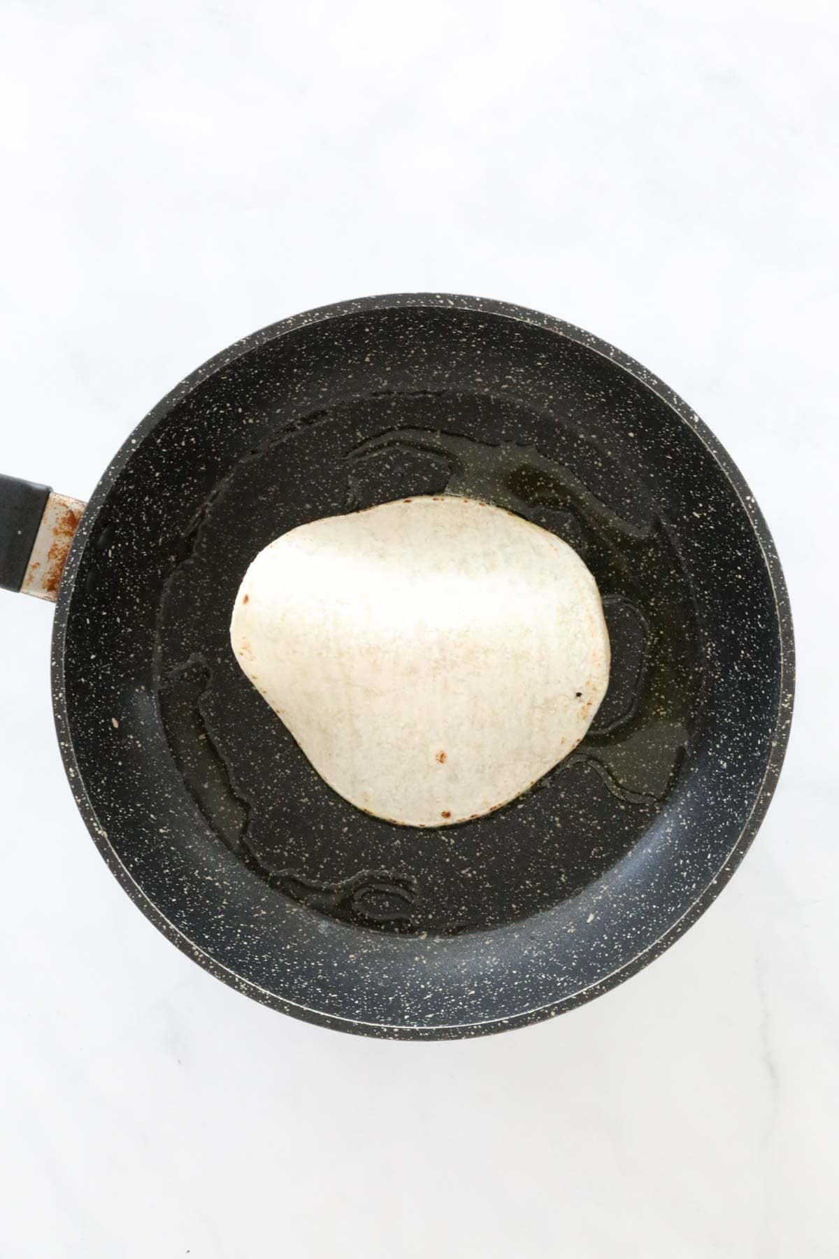 A tortilla in a frying pan, minced beef side facing down.