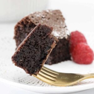 A moist and rich chocolate cake on a gold fork with raspberries in the background.