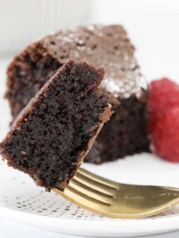 A moist and rich chocolate cake on a gold fork with raspberries in the background.