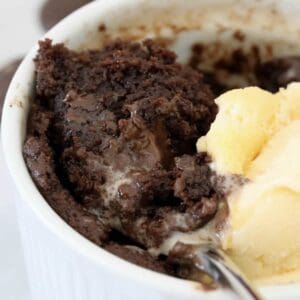 A gooey chocolate cake in a mug with vanilla ice cream.