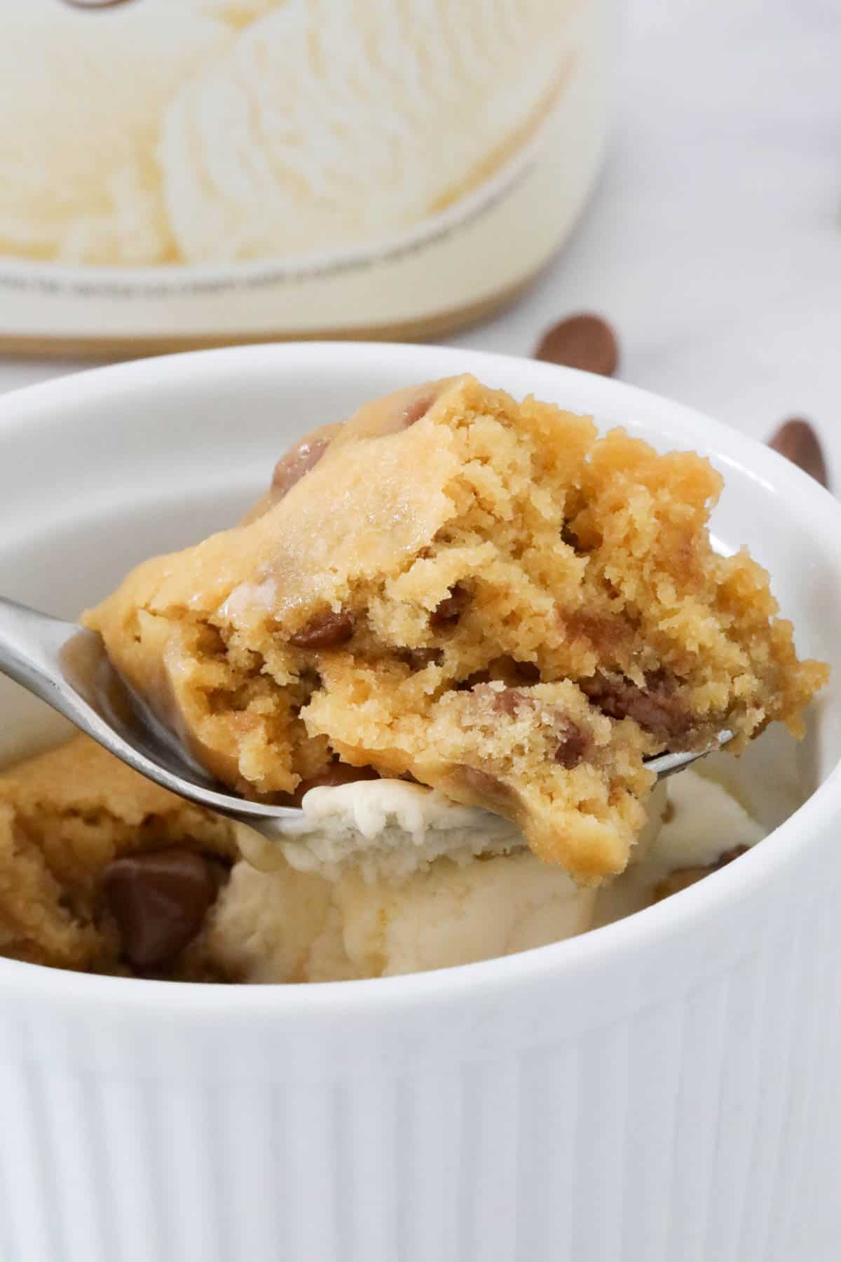 A spoon holding mug cake above a ramekin.