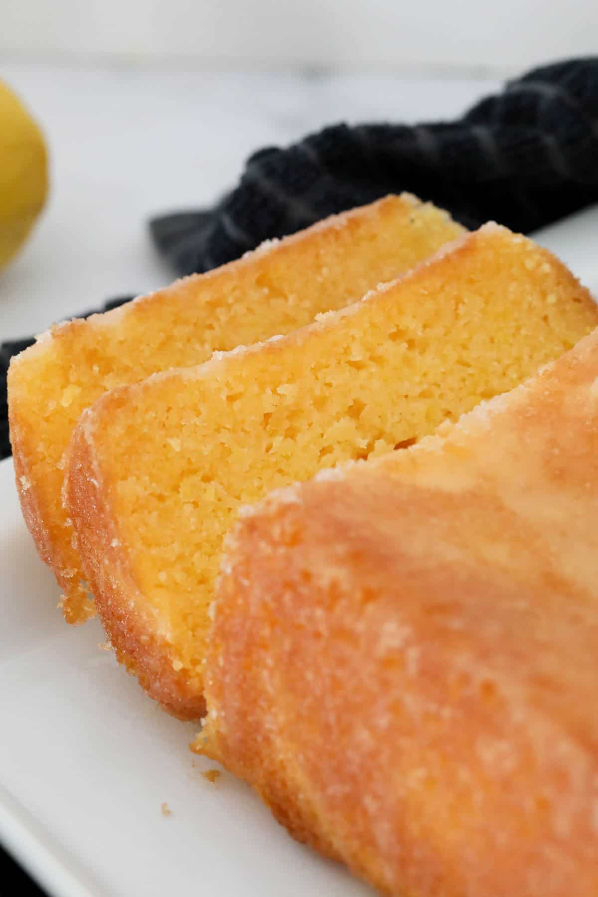 Gluten free lemon drizzle loaf cake sliced and placed on a white platter.