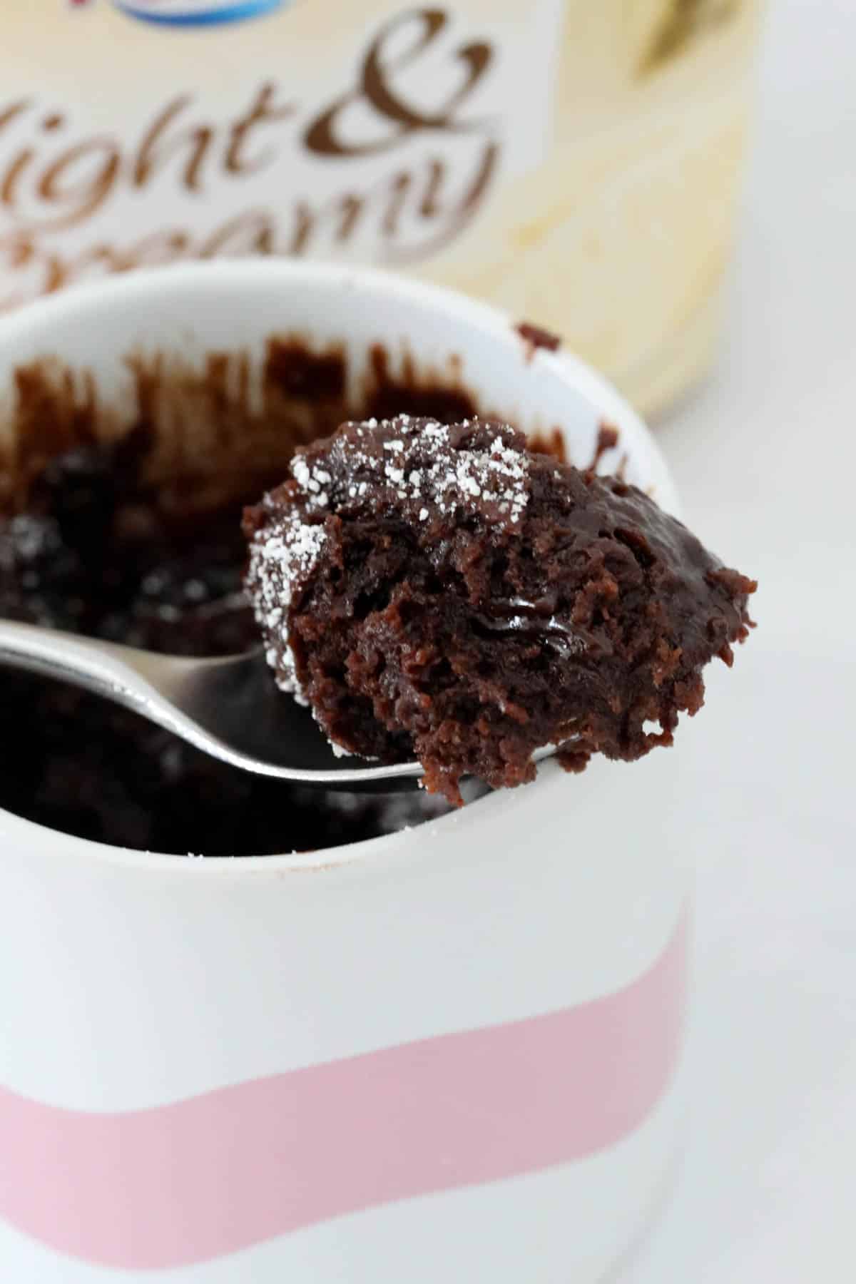 A spoon above a small white ramekin of fudgy gluten free chocolate mug cake.