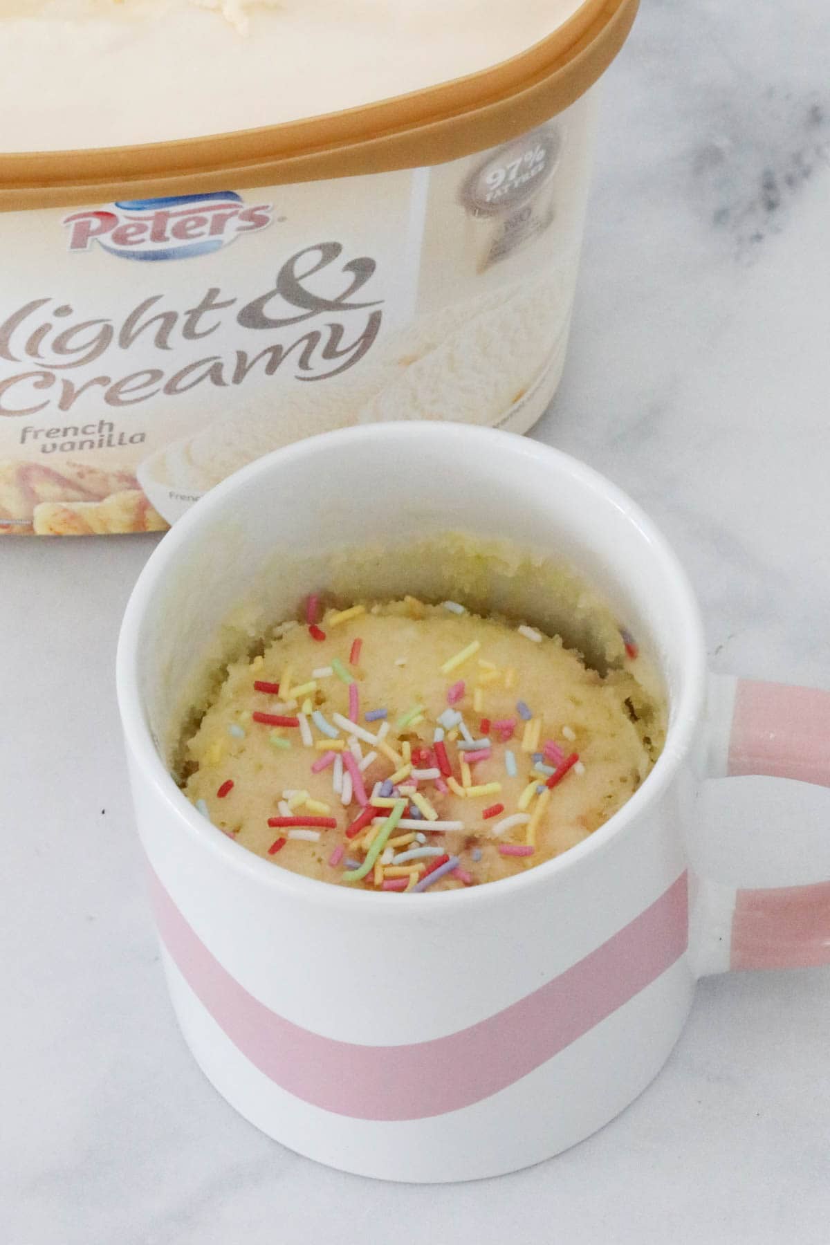 A vanilla mug cake in front of a tub of vanilla ice cream.