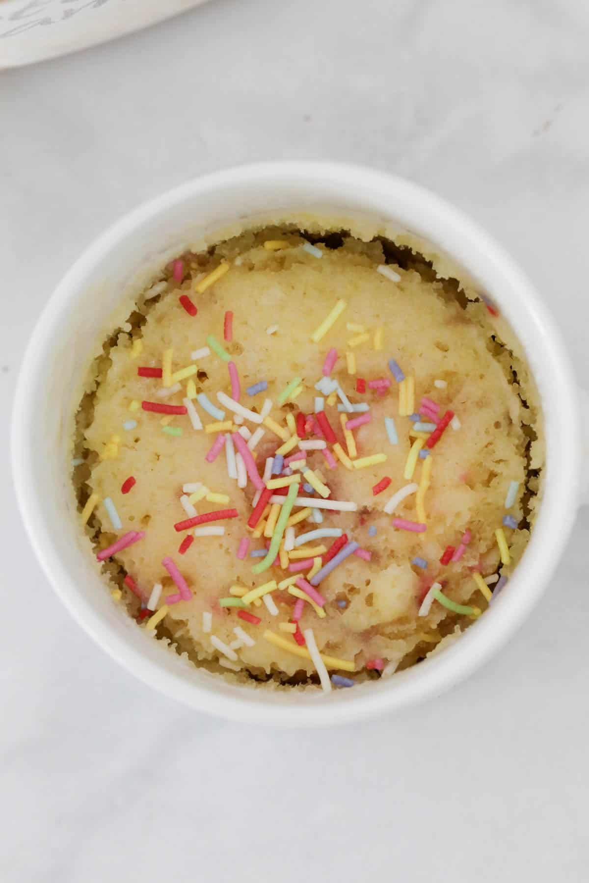 Overhead shot of gluten free vanilla mug cake with sprinkles on top.