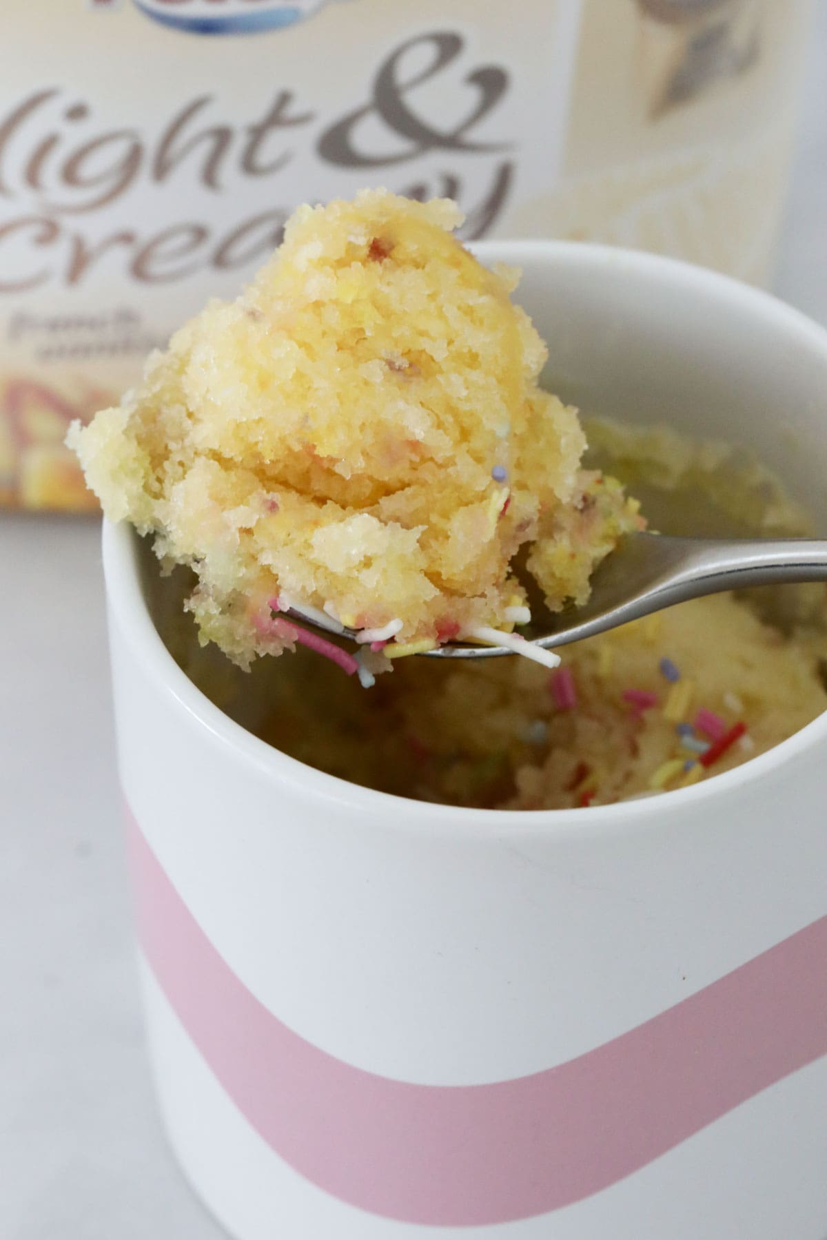 A spoon lifting some vanilla cake out of a pink and white mug.