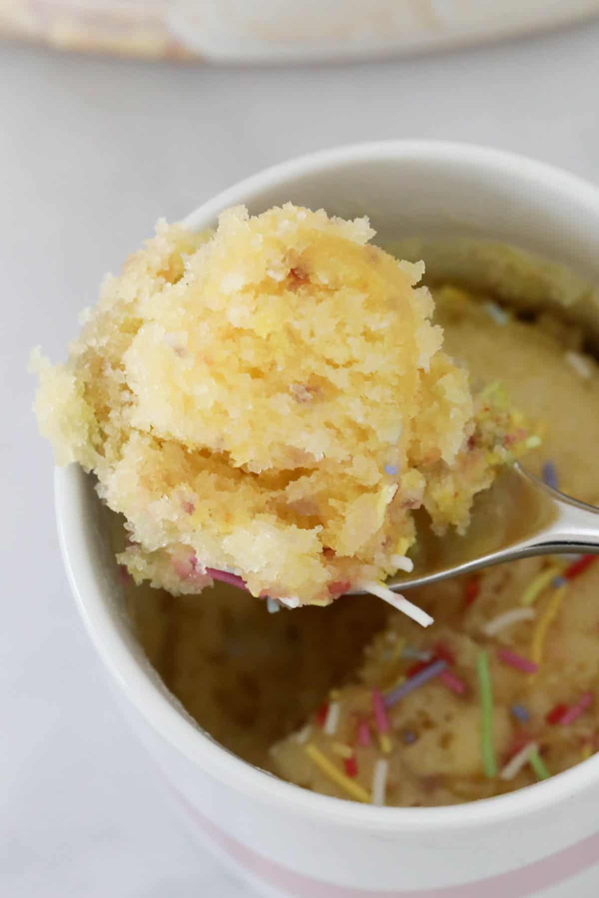 Close up of gluten free vanilla mug cake on a spoon held above a mug.