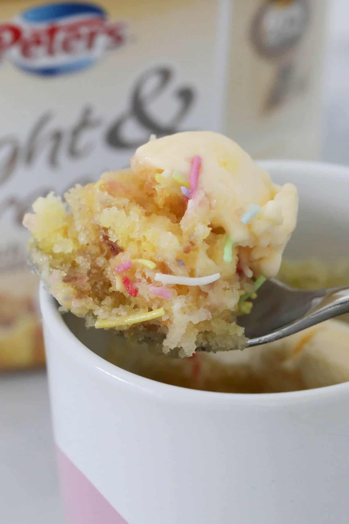 Close up of vanilla mug cake, sprinkles, and ice cream on a spoon.