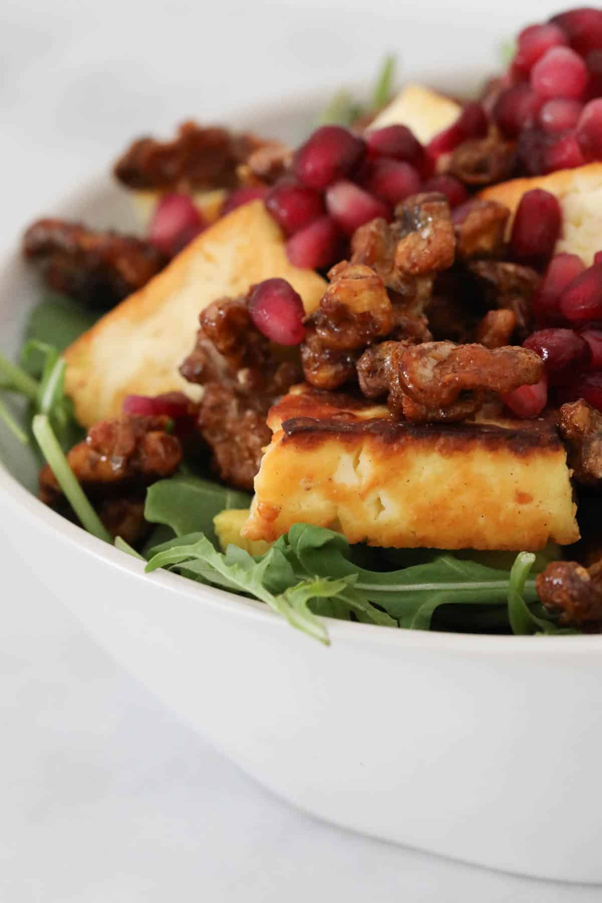 Side view of golden pan-fried halloumi cheese, honeyed walnuts and red pomegranate seeds, on top of the rocket salad.