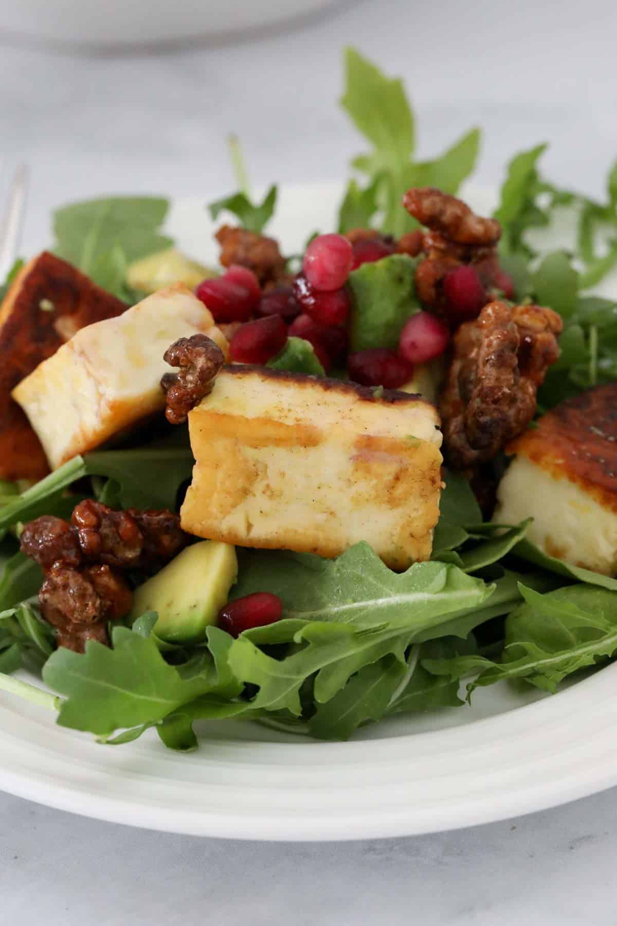 A serving of halloumi salad topped with walnuts and juicy pomegranate seeds.