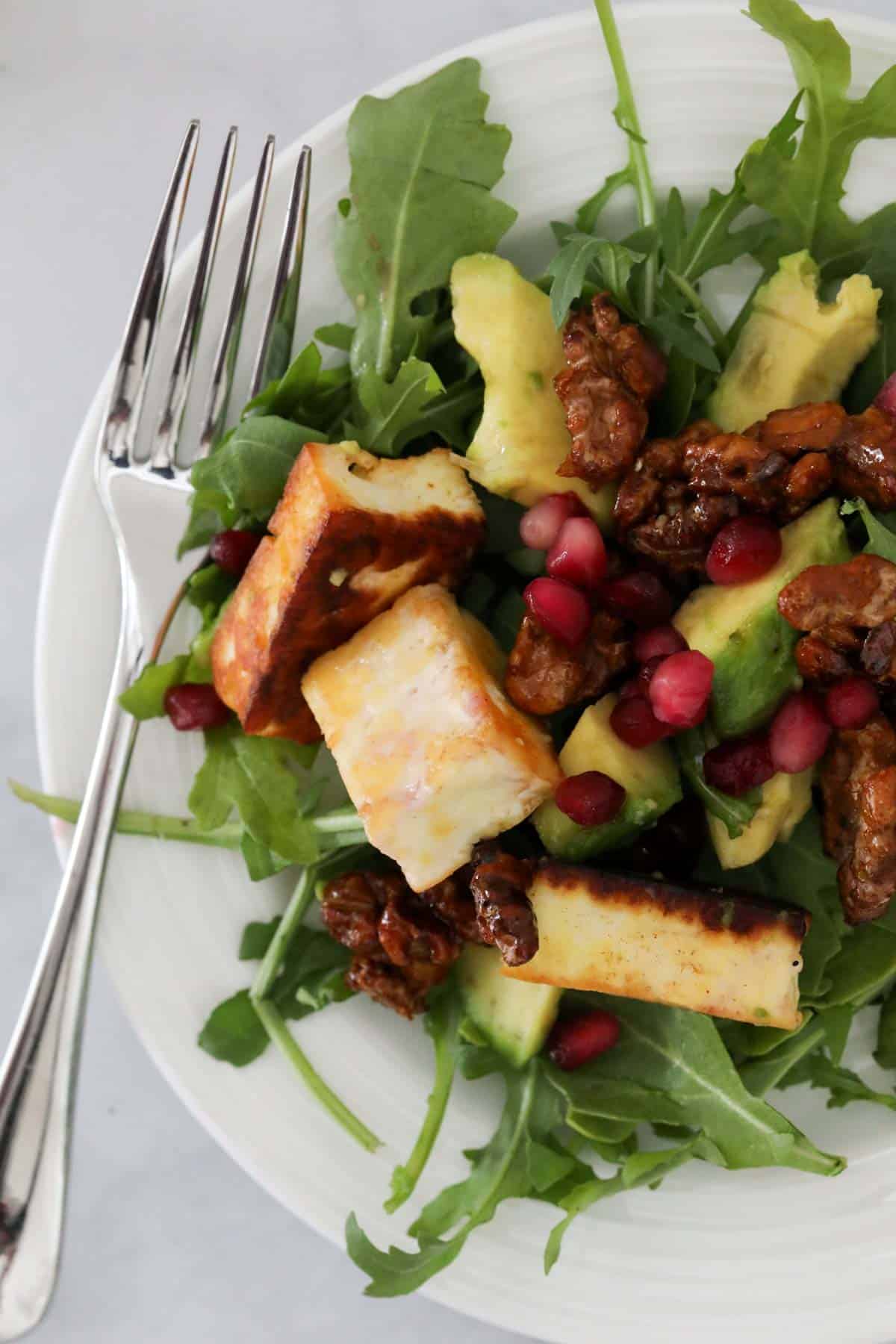 A serving of halloumi and pomegranate salad on a white plate with a fork to the left hand side.