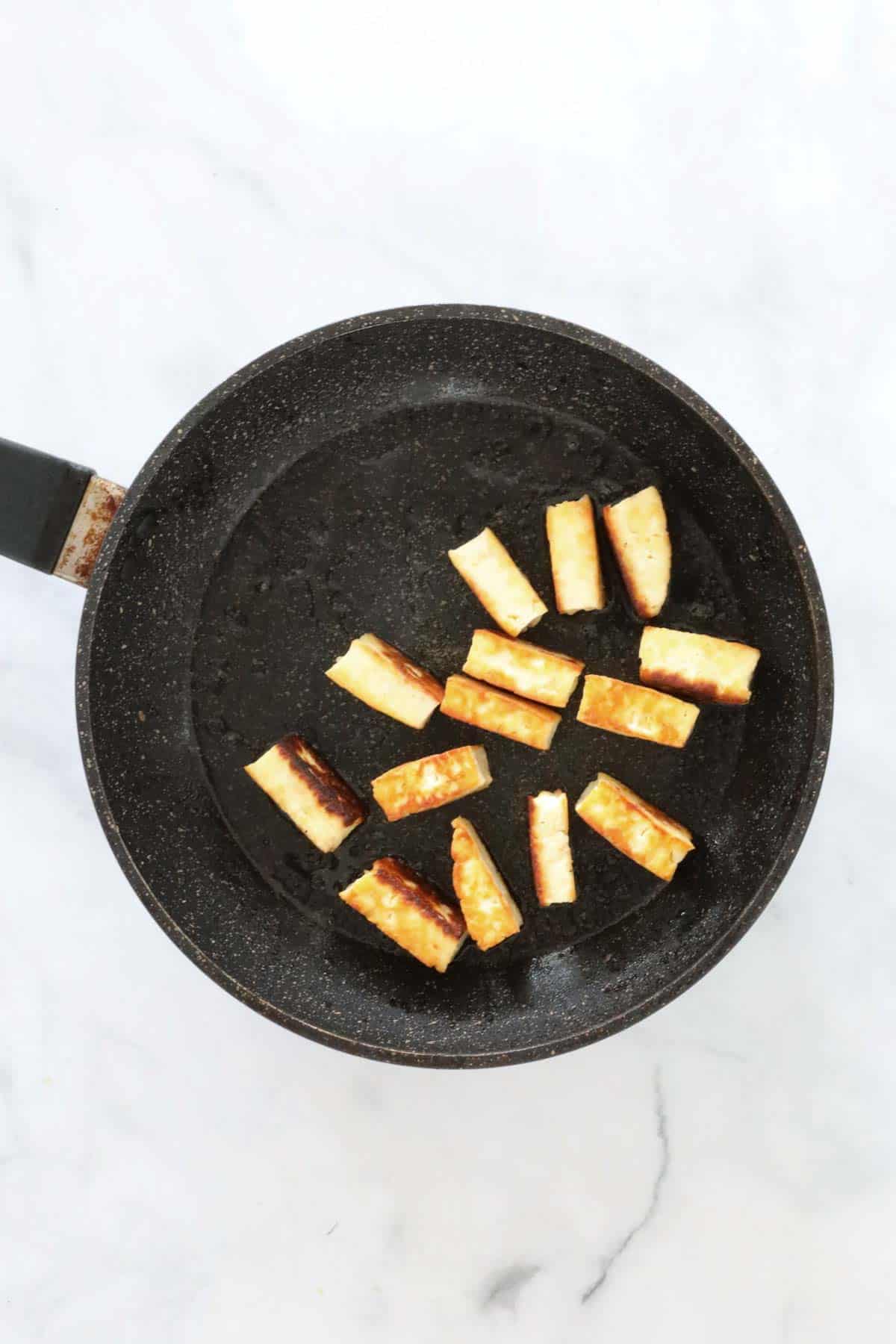 Slices of golden halloumi cheese in a frying pan.