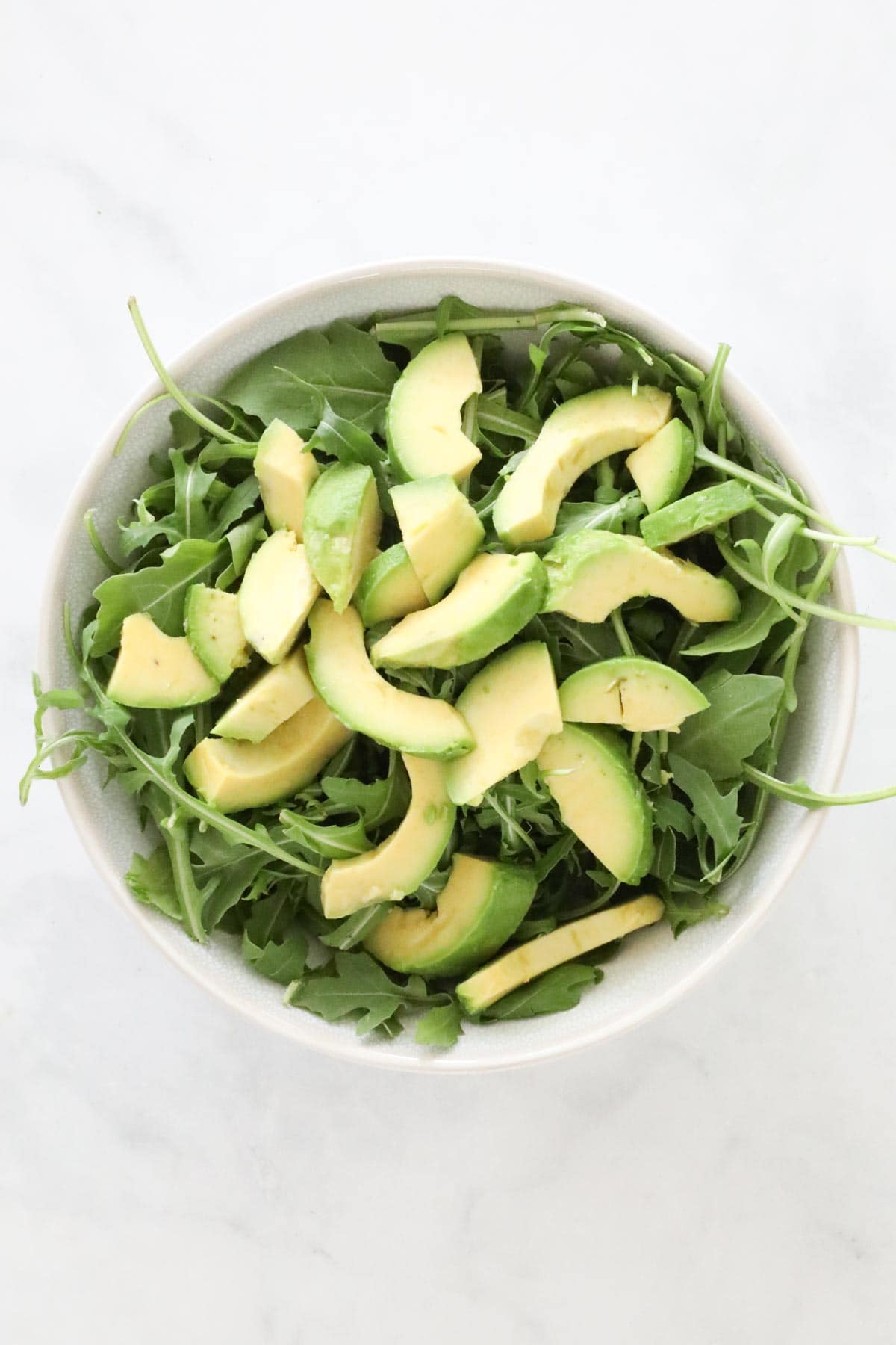 Rocket topped with sliced avocado in a serving bowl.