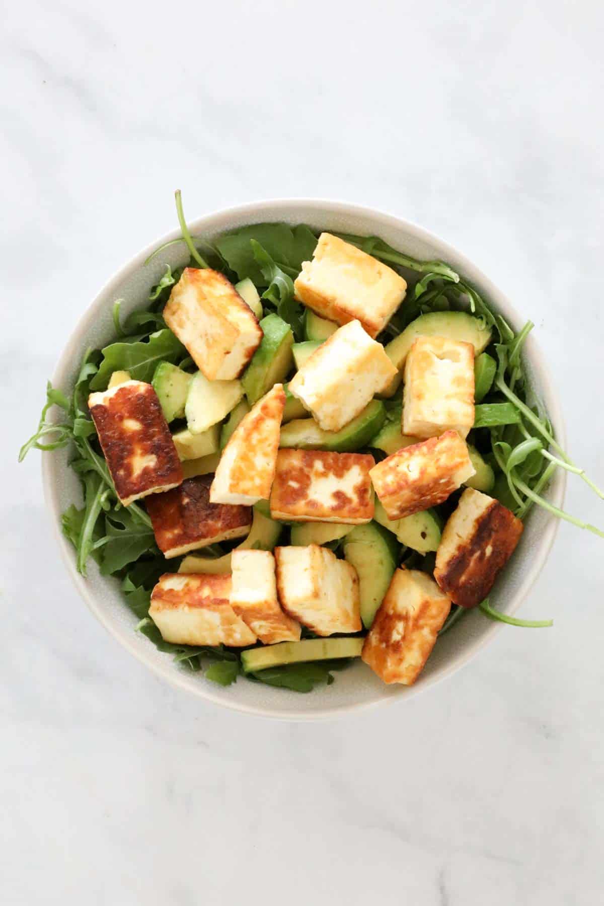 Golden fried halloumi placed on top of the avocado and rocket.